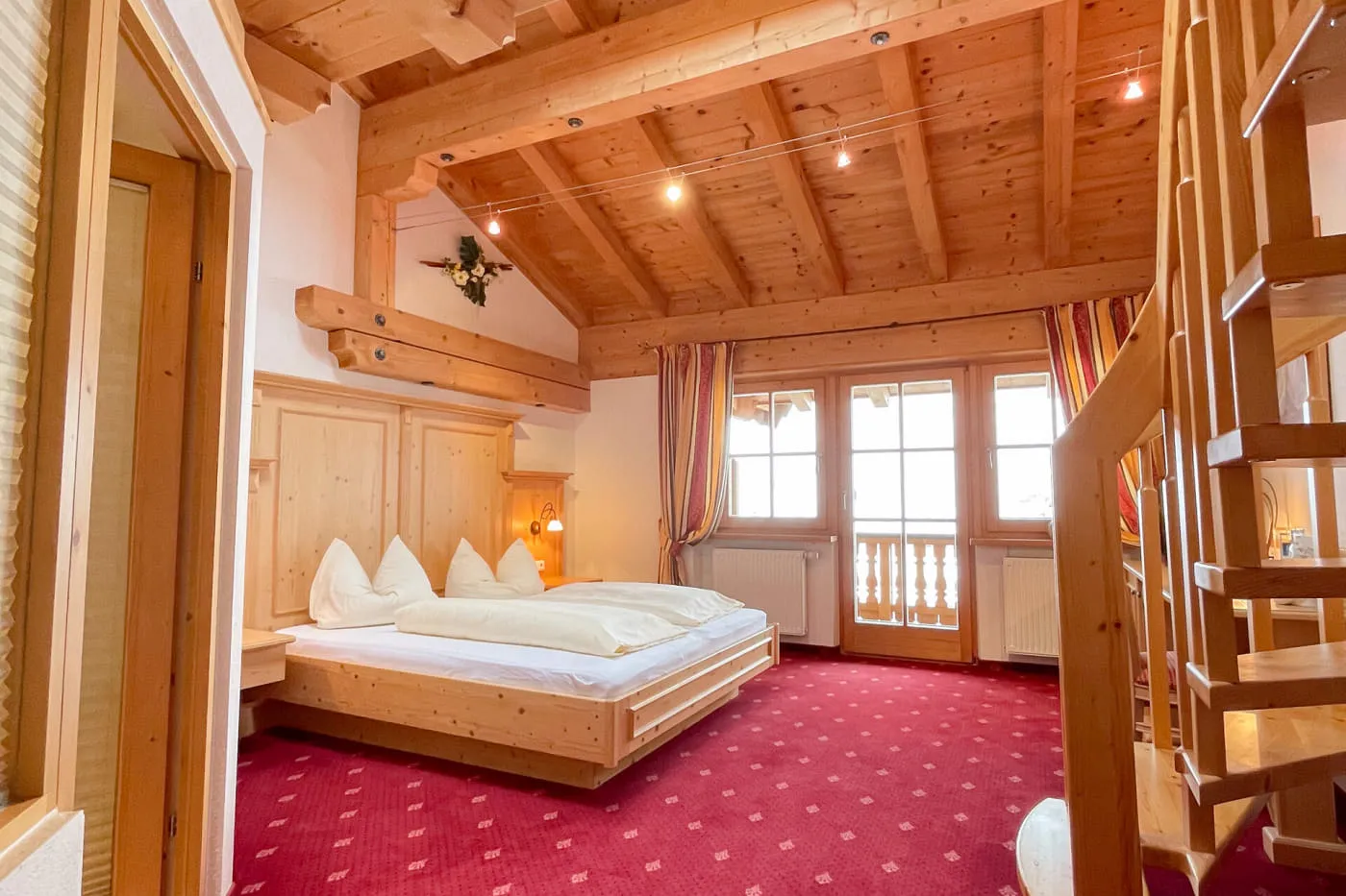 Schlafbereich der Suite Ochsalm mit Doppelbett, Holzdecke, Balkon und Treppe zur Galerie